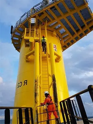 employees climbign ladder to reach the top of wind turbine rig